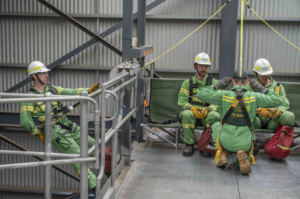 Two people sitting with one person preparing to rappel off the side of a high internal tower 