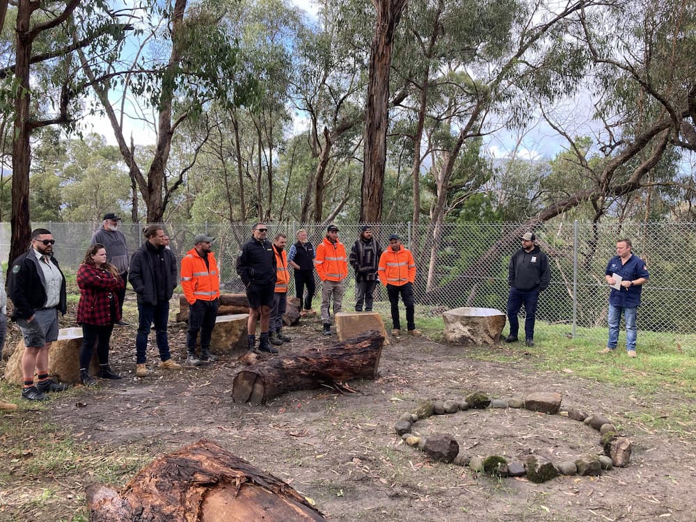 Group of people standing in cleared bush with logs and rocks