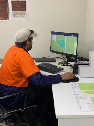 Man wearing orange shirt with blue sleeves and white cap on head sitting at a computer